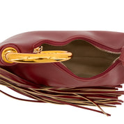 Close-up of a burgundy leather handbag with a gold-tone metal handle and a long fringe detail, shown open against a white background.