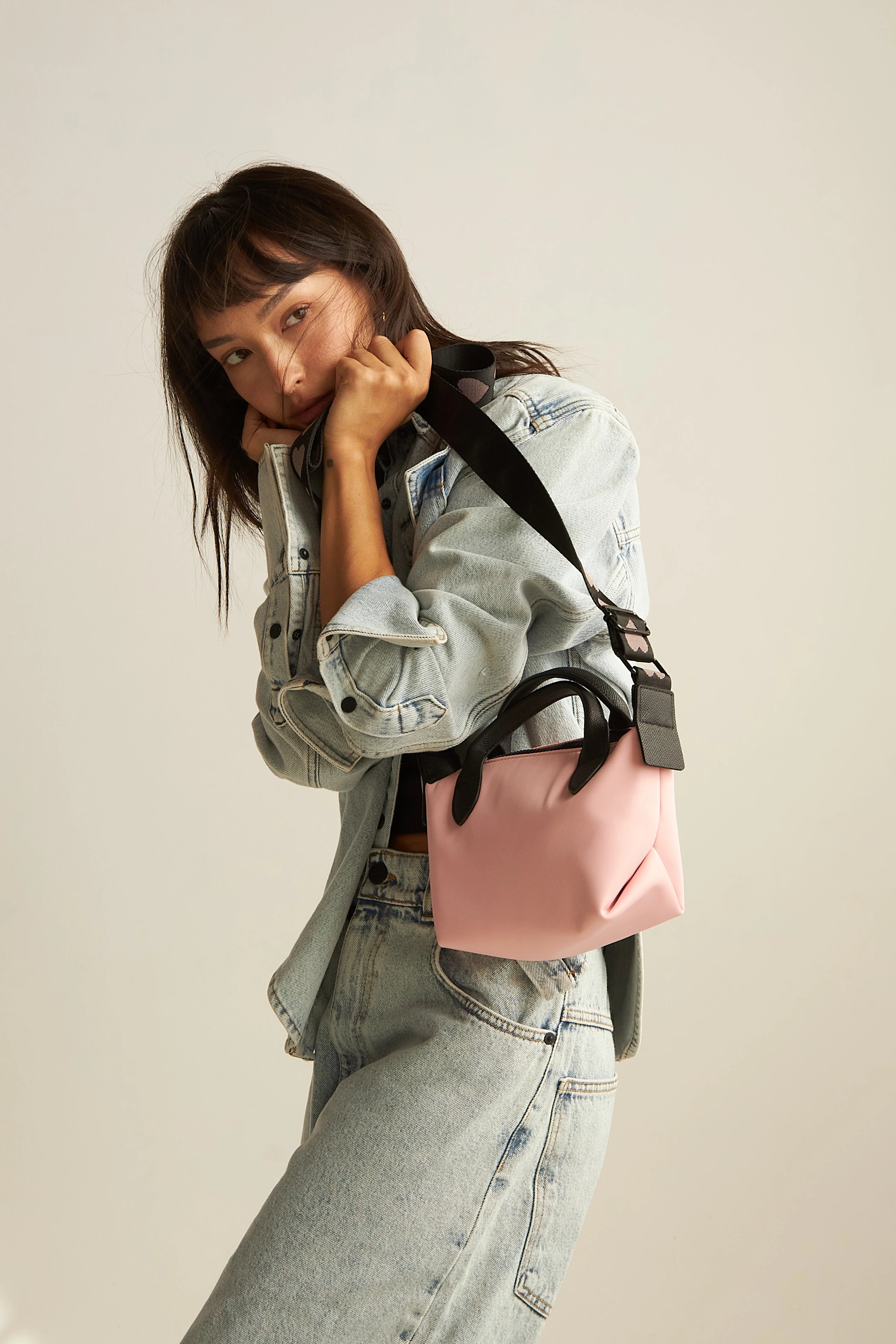 A model is holding a pink crossbody bag.