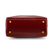 The bottom corner of a Wine  crocodile-embossed leather handbag, showing gold-tone metal studs on a white background.