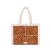 A small structured tote bag with cream-colored plush faux fur trim and handles, featuring a front panel made of four brown animal-print panels with white spots, resembling deer or cowhide.