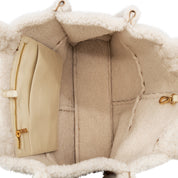 Close-up interior view of a cream-colored bag with a plush sherpa lining and a beige zippered pocket with gold-tone hardware.