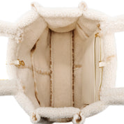 Close-up of the interior of a cream-colored teddy fleece or shearling bag, showing padded compartments, zipper details, and a smooth lining.