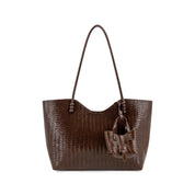 A dark brown woven leather tote bag with a matching leather hanging charm, displayed against a solid white background.